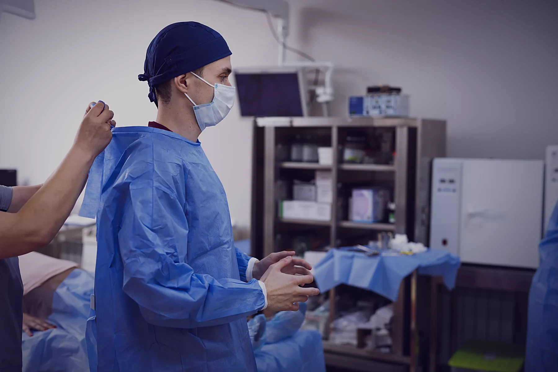 A surgeon being gowned by a colleague before surgery